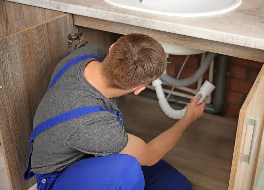 Professional plumber in uniform fixing sink using putty